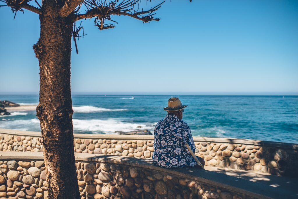 Elderly Senior Citizen sitting at ocean beach watching waves