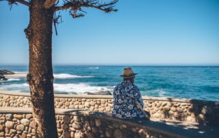 Elderly Senior Citizen sitting at ocean beach watching waves