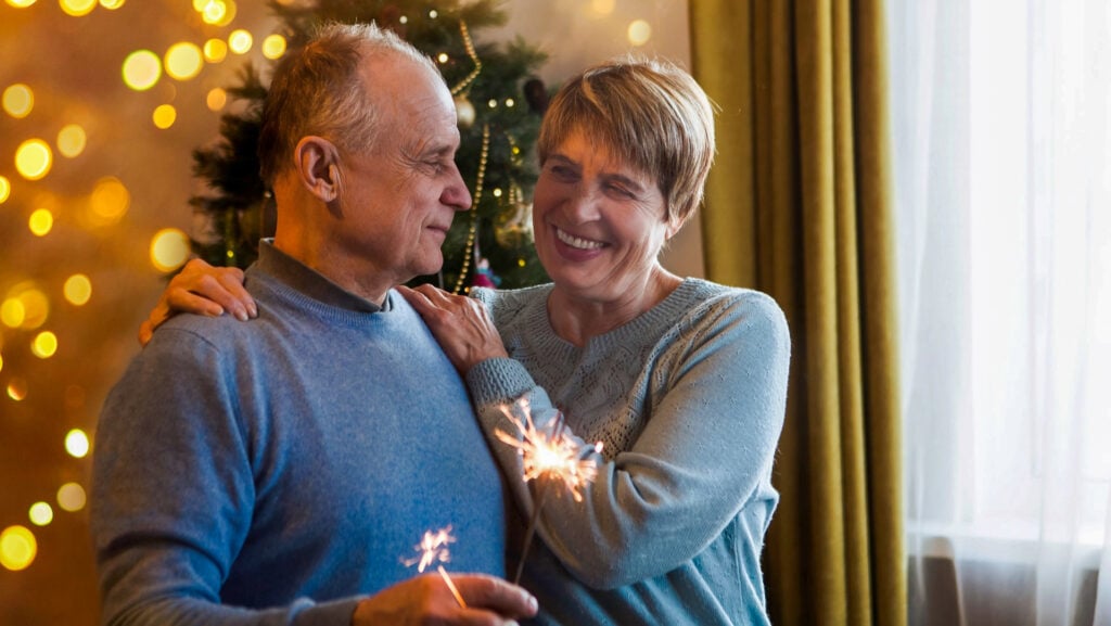 Elderly senior couple on new years eve with sparkler and christmas tree