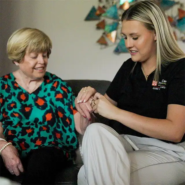 photo of an older woman on the left with her hand extended as the younger woman on the right, wearing a black HomeCare Advocacy Network polo shirt, assists her with the ring on her finger