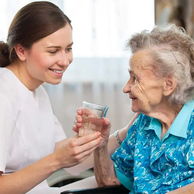 photo of a young woman on the left helping an elderly woman on the right with a glass of water