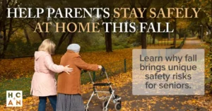 Adult daughter walks beside an older woman using a rollator on a leaf-covered park path in autumn, illustrating fall safety support for seniors aging at home.
