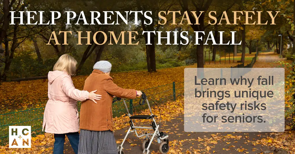 Adult daughter walks beside an older woman using a rollator on a leaf-covered park path in autumn, illustrating fall safety support for seniors aging at home.